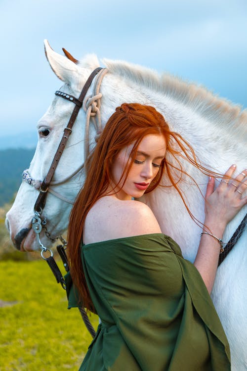 free-photo-of-redhead-woman-posing-near-white-horse-in-nature